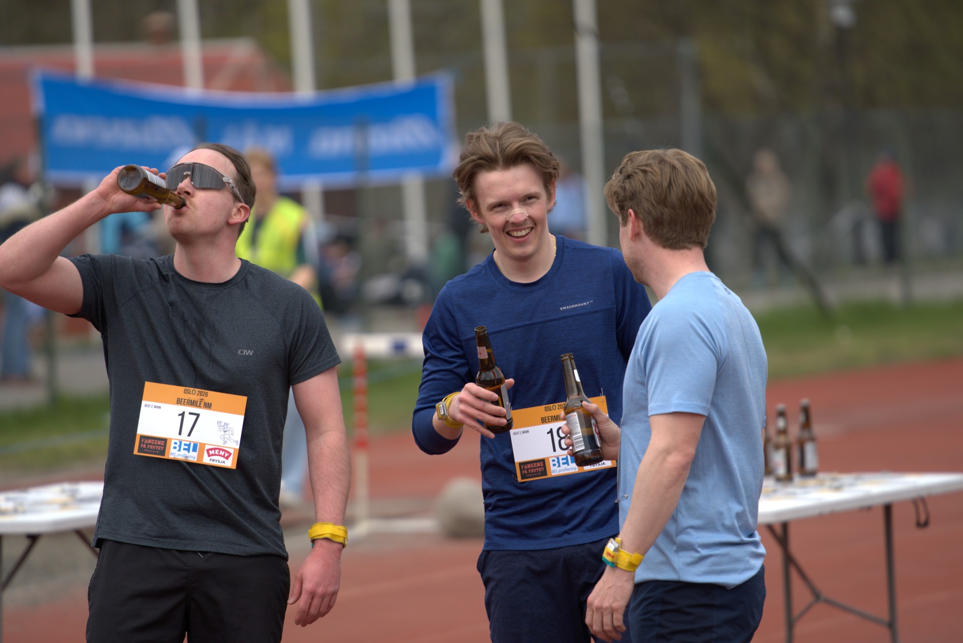 Tre løpere ler og drikker øl sammen i drikkesonen under NM i Beermile 2026